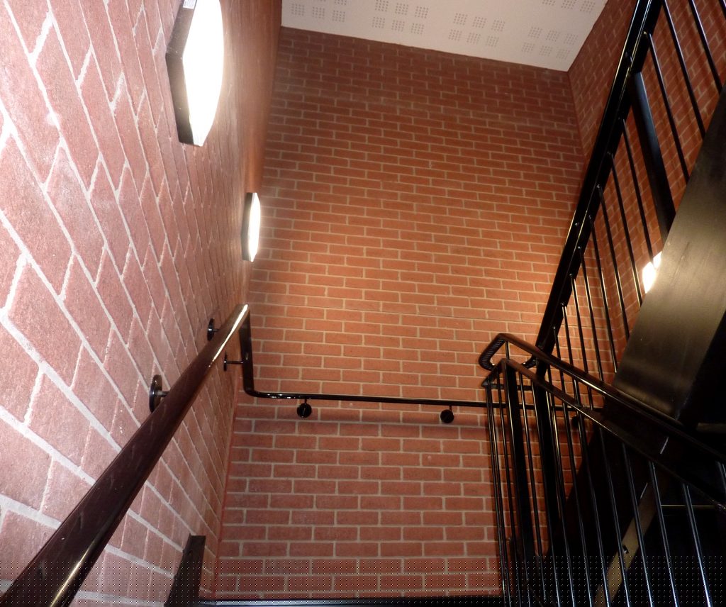 A stairwell with glossy black stairs and railings, set against brick-effect cladded walls