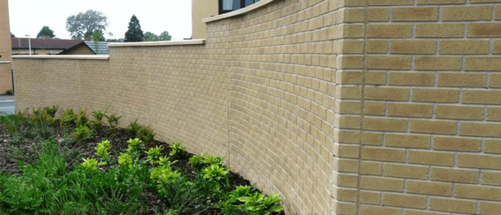 Property walls covered with light-coloured brick-effect cladding next to a flower bed